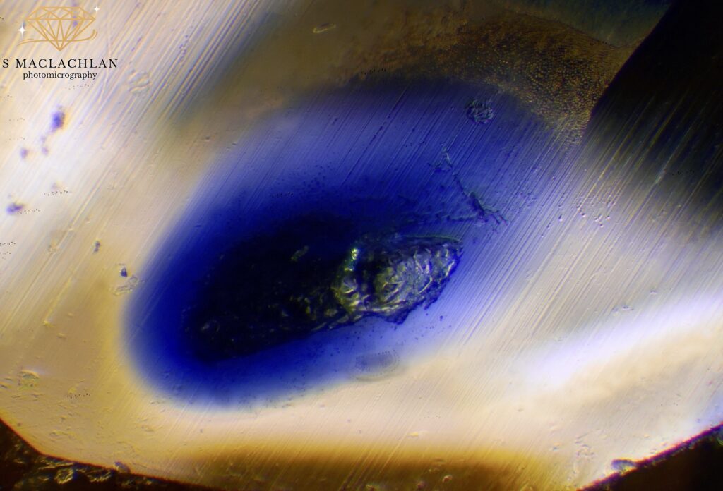 Foto 4: L’immagine qui riportata è una fotomicrografia di un alone blu trovato in questo zaffiro giallo/arancio diffuso al berillio. Naturalmente, questi aloni non sono diagnostici della diffusione al berillio, ma del trattamento termico ad elevate temperature, che provoca la diffusione interna di inclusioni contenenti titanio, come il rutilo, dando origine a questi splendidi aloni blu. Si tratta di una sovrapposizione di 23 immagini in stacking. Ingrandimento 120x