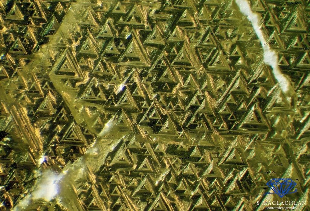 Foto 5: Qui sono rappresentati i trigoni sulla faccia ottaedrica di un cristallo di diamante giallo. Si tratta di una sovrapposizione di 15 immagini in stacking con un ingrandimento di 120x